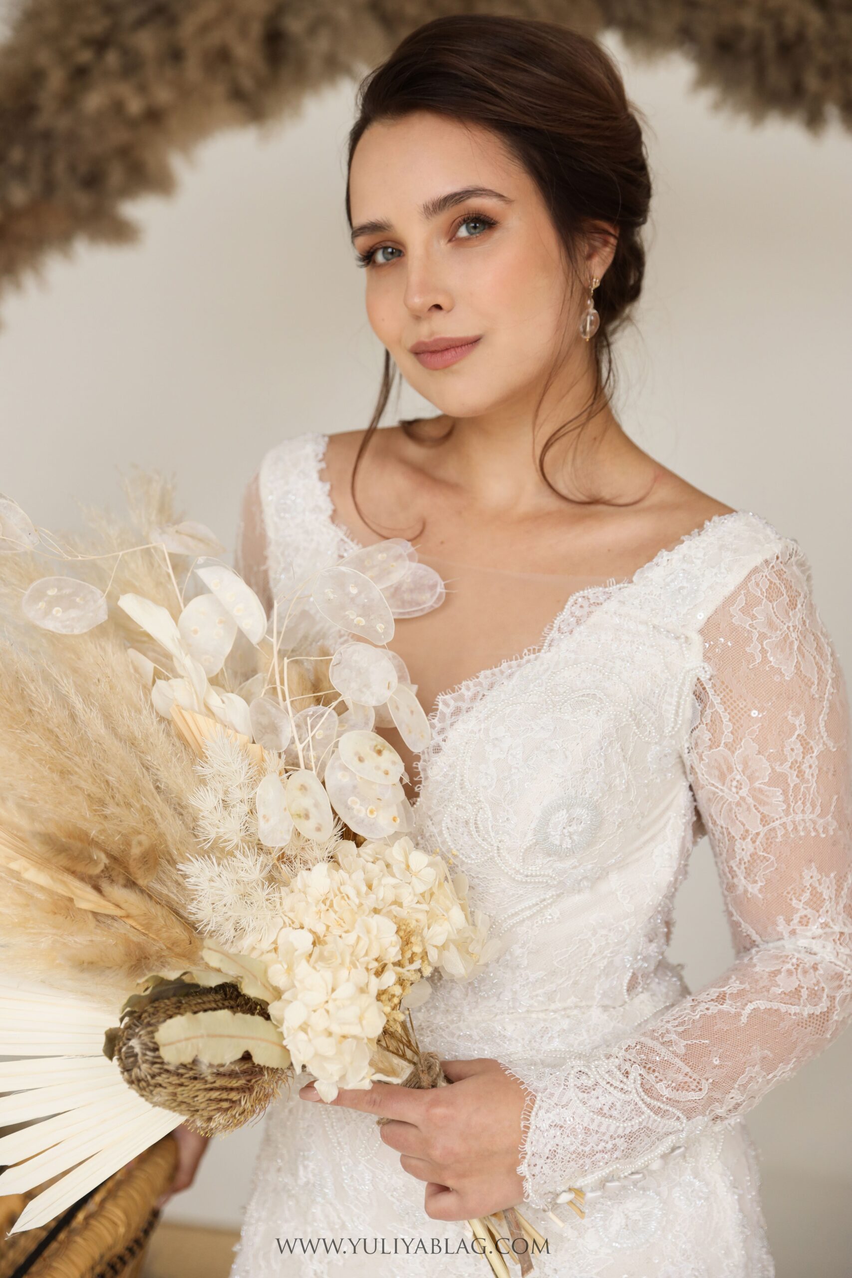 A portrait of a bride in Montreal, her bridal makeup soft and natural, holding a unique bouquet of dried flowers and pampas grass, with her lace gown adding a touch of timeless elegance