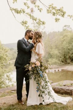 A romantic outdoor wedding moment in Montreal with the bride and groom sharing a kiss, the bride’s hair adorned with flowers complementing her flowing wedding dress, styled by Beauty Trend