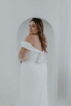 A confident bride in a modern off-shoulder wedding gown posing in a minimalist setting, with a naturally styled wavy hair look created by a Beauty Trend wedding makeup artist in Montreal