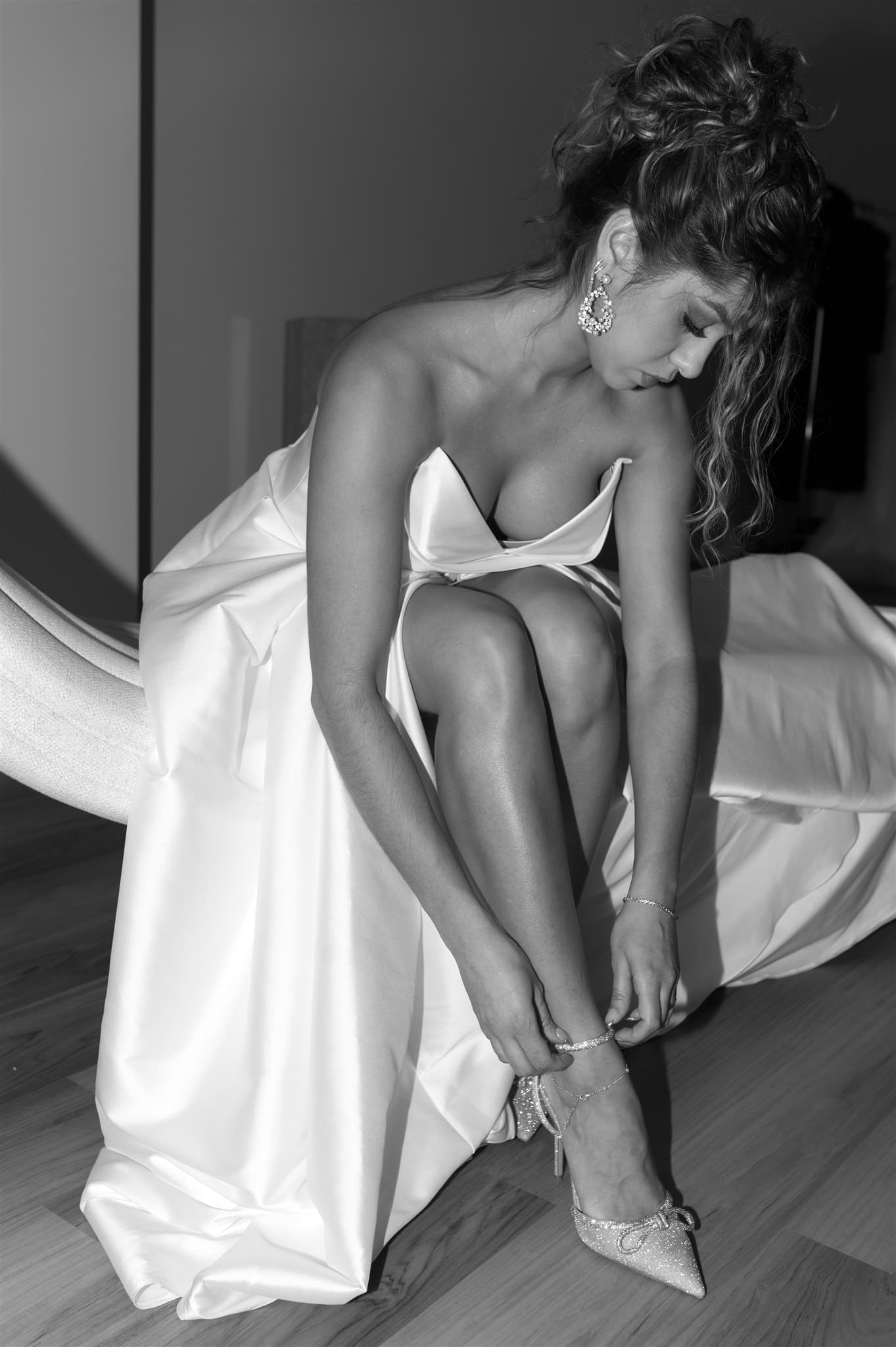 A black-and-white photo of a Montreal bride adjusting her shoes, styled by bridal hair and makeup experts for an elegant wedding look.